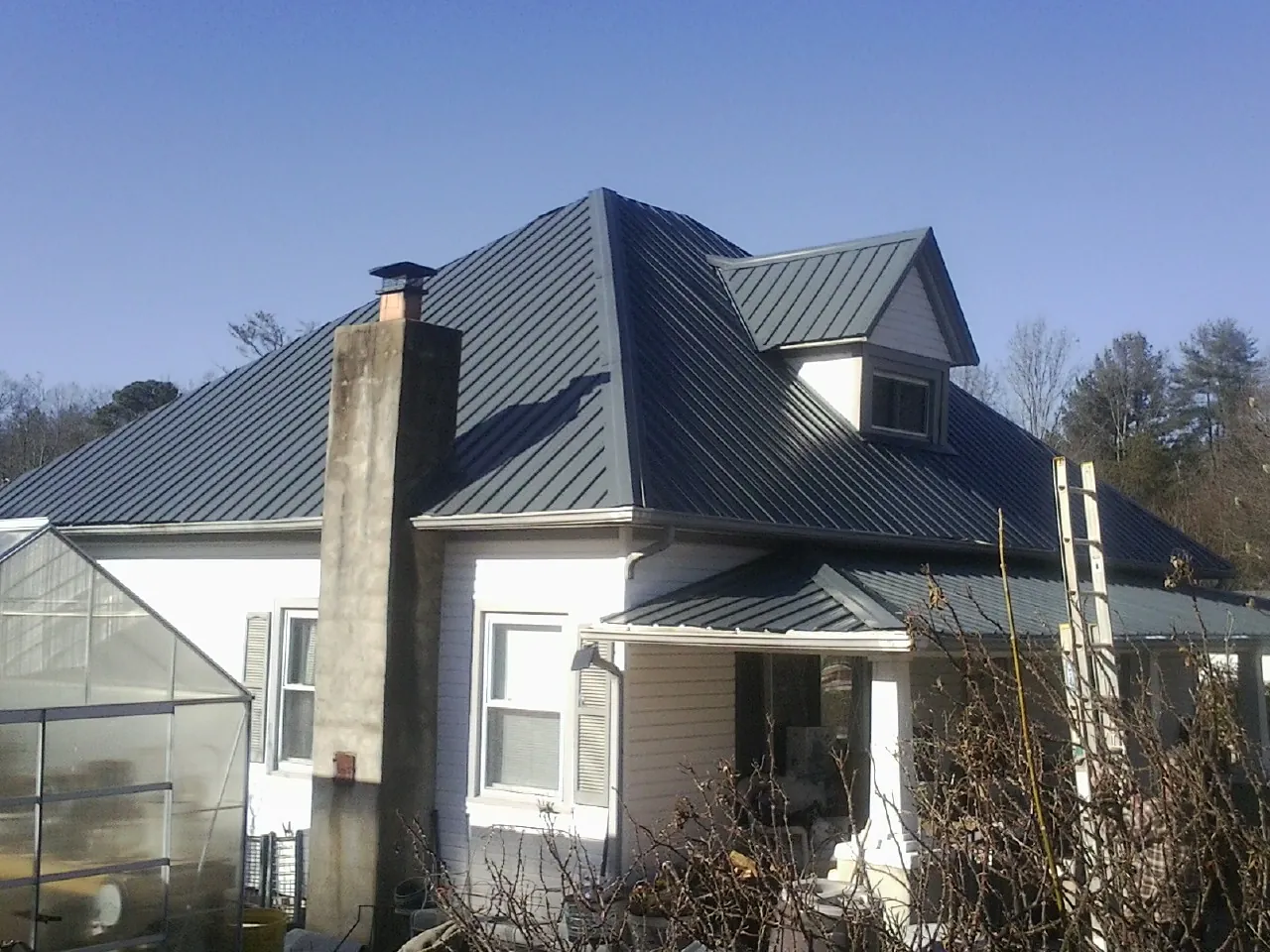 Dark blue standing seam metal roof on a white farmhouse with dormer — Slate & Tile Roof Repair by Roofing Brothers in Cerro Gordo
