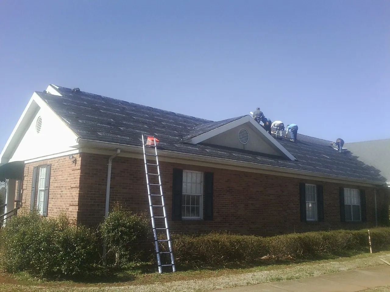 Crew tearing shingles off a brick ranch roof with a ladder set — Emergency Roof Repair work by our crew in Cerro Gordo