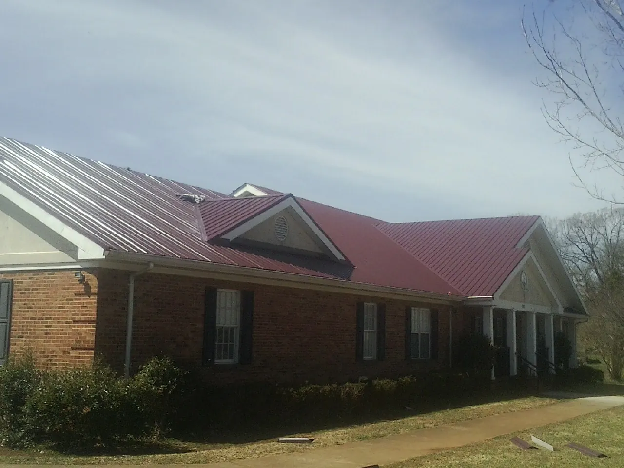 Red metal roof with gabled entries on a long brick building, from a Hail Damage Roof Repair job in Cerro Gordo