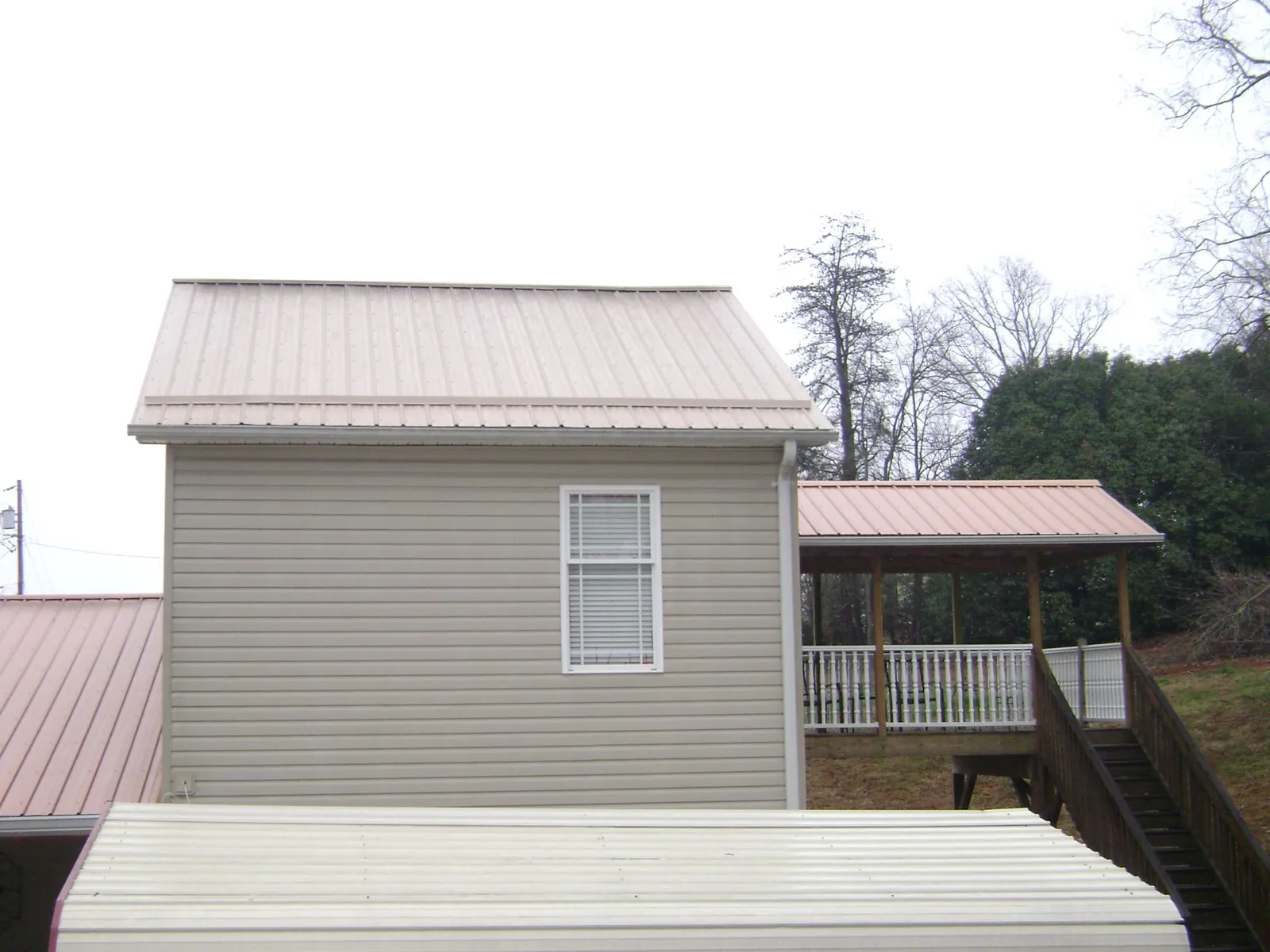 Tan metal roofs on a two story addition and attached porch, from a Roof Replacement job in Cerro Gordo