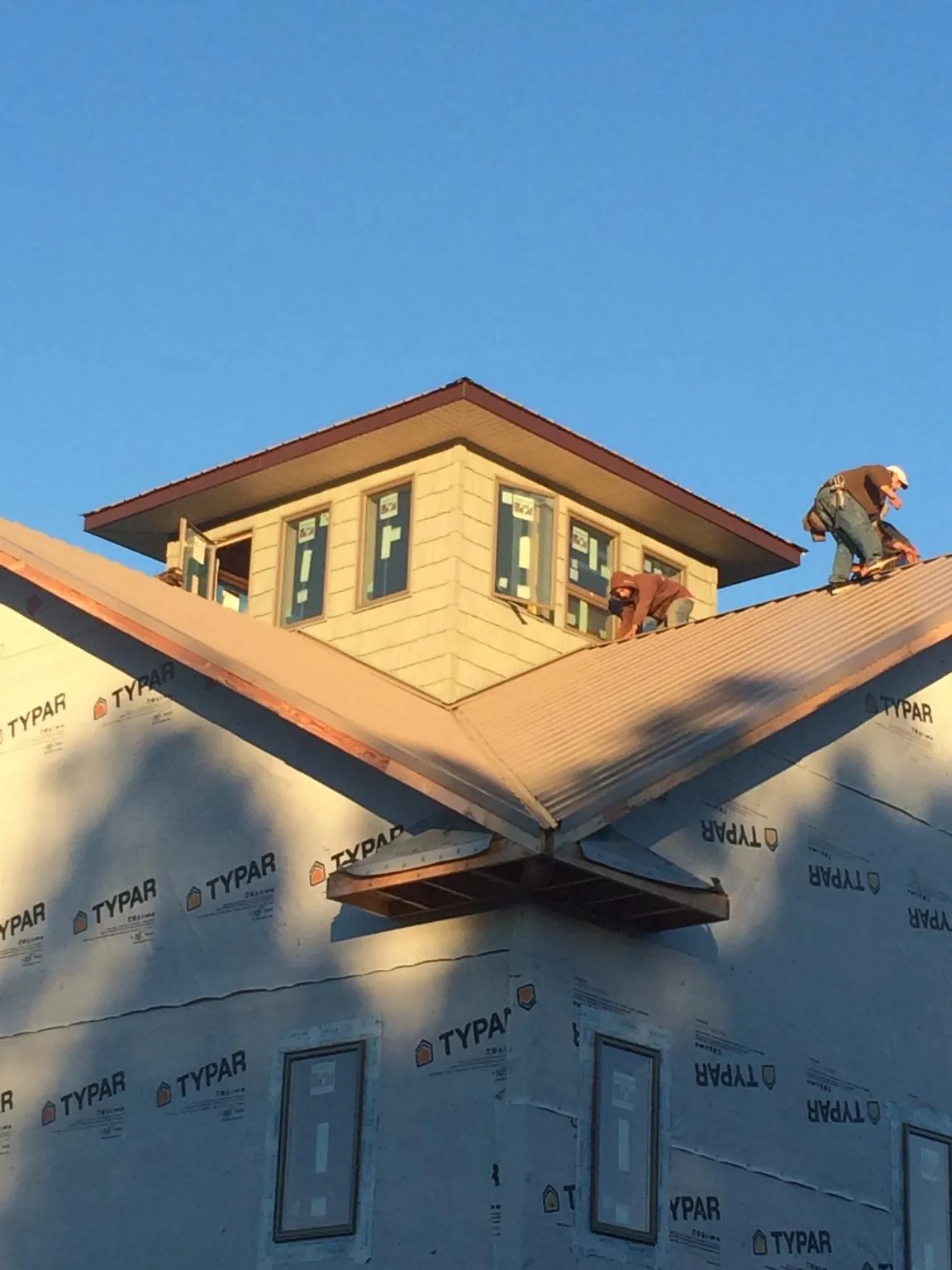 Roofers working around a rooftop cupola on a new metal roof at sunset — Roof Waterproofing in Cerro Gordo by Roofing Brothers